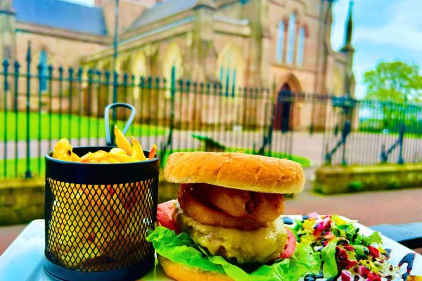 Image shows a burger and fries dish. Church is in the background.