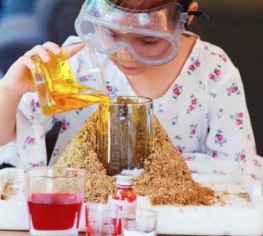 Kid science experiment of volcano or Baking Soda and Vinegar Volcano Eruption for Kid.Girl with eyeglasses pouring dish soap to the  container of baking soda,mixed and poring vinegar for volcano labs.
