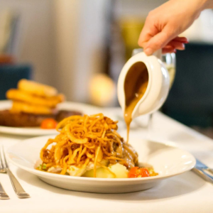 Image of sauce being poured onto meat topped with crispy onions