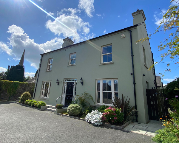 Bramley House 5 bedroom house painted a pale green with a black door. There is plenty of greenery around the front of the house and it is pictured on a beautiful sunny day.