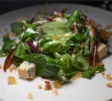 Plate of mixed green salad with leafy greens, cheese, and toppings on a white dish.