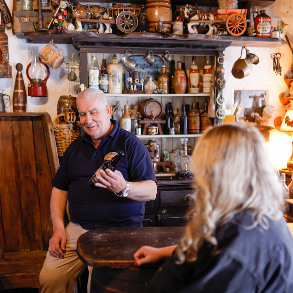 Colin Winter speaking inside Dan Winter's Cottage, with shelves of vintage items and bottles in the background.