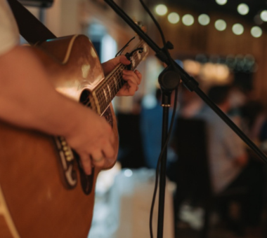 Close-up of a person playing an acoustic guitar beside a microphone at the Orchard Hooley in Long Meadow Cider's Bramley Barn.