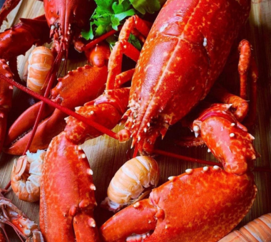 Cooked lobsters arranged on a wooden board with herbs, ready to serve.