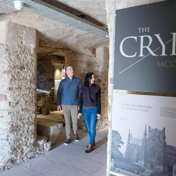 Stone crypt interior beneath St Patrick’s Church of Ireland Cathedral in Armagh, with two visitors walking through.