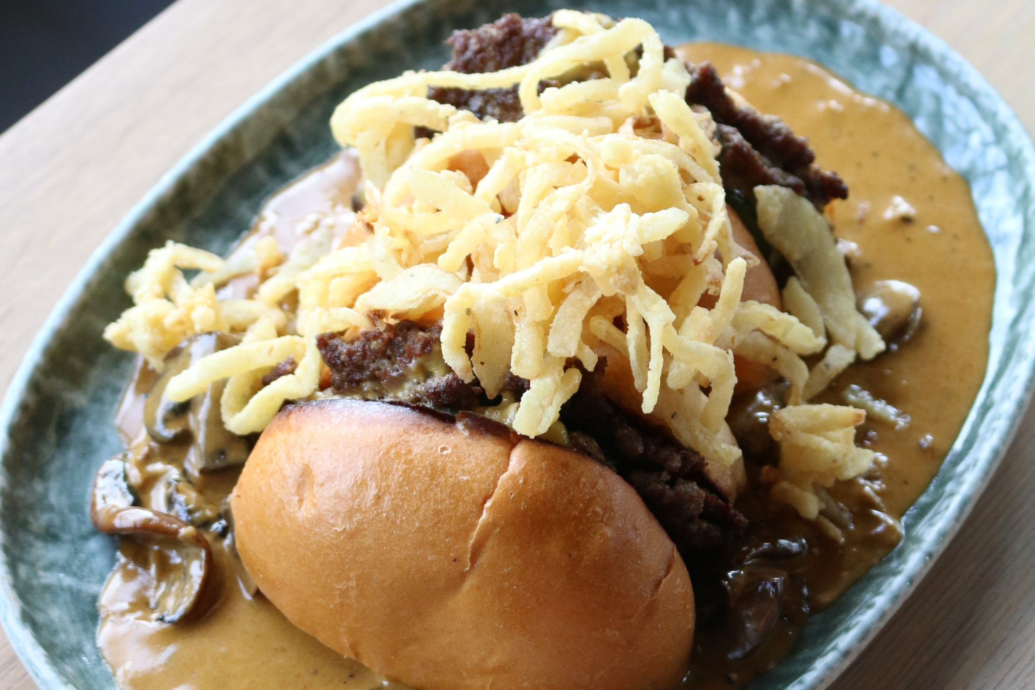 Blend & Batch Buskfest Offer Close-up of a loaded beef burger with locally sourced Quail’s Butcher beef, double American cheese, dill pickles in a brioche bap, topped with crispy onions and served over stroganoff sauce with fries.