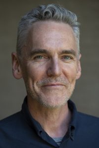 Close-up portrait of Ian McBride. A man with short grey hair and light stubble against a neutral background.