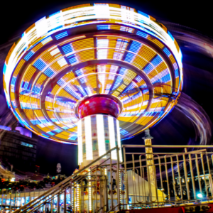 Colourful illuminated fairground swing ride spinning at night, with bright lights creating motion trails
