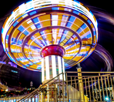 Colourful illuminated fairground swing ride spinning at night, with bright lights creating motion trails