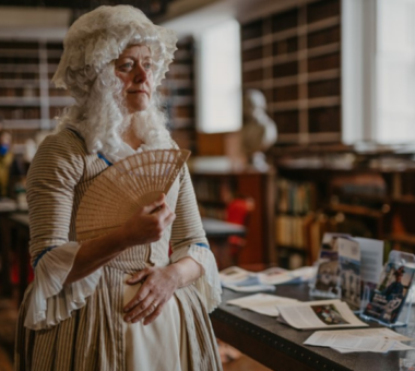 Person in Georgian period costume holding a folding fan during an event at Armagh Robinson Library as part of the Armagh Georgian Festival.