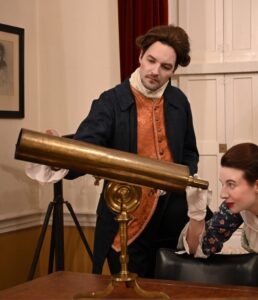Two people in Georgian period costume examining a brass telescope during a historical interpretation experience at the Armagh Observatory.