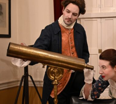 Two people in Georgian period costume examining a brass telescope during a historical interpretation experience at the Armagh Observatory.