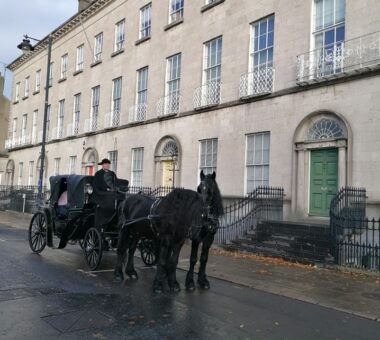 Horse-drawn carriage parked outside a row of Georgian townhouses in Armagh city, with two black horses and a carriage driver