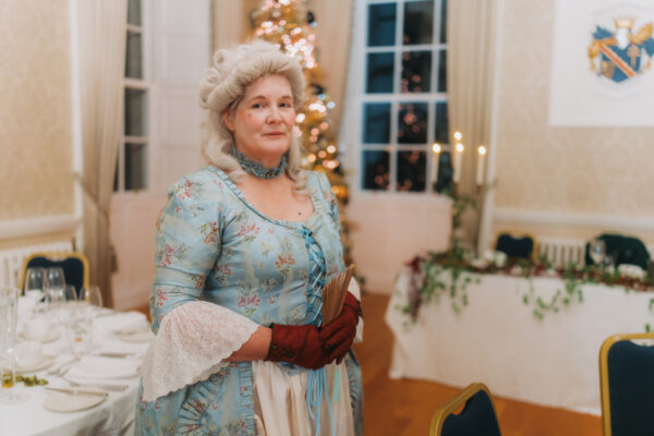 Armagh Georgian Festival - Banquet Image Performer in Georgian-era costume standing in a festively decorated banquet room during a Georgian Christmas dining experience at the Armagh Georgian Festival.