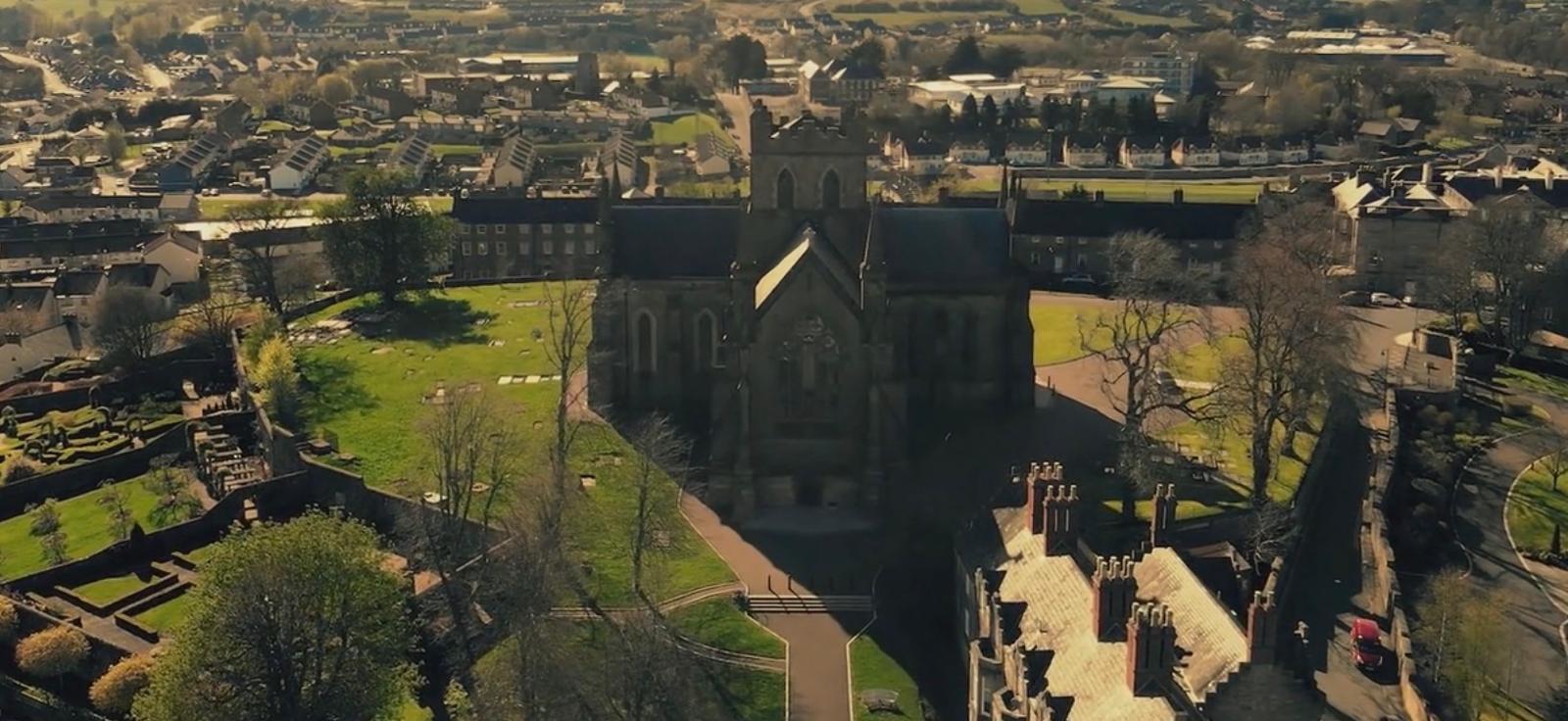 Aerial view of St Patrick’s Church of Ireland Cathedral on the Hill of Armagh, surrounded by historic buildings, cathedral gardens and the city skyline.