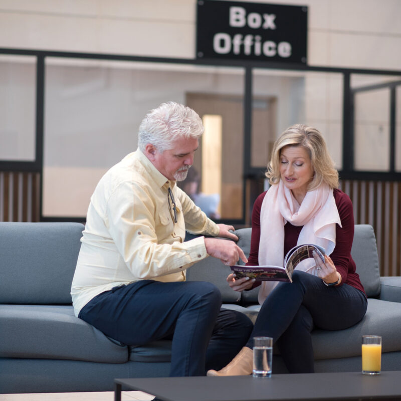 Visitors relaxing in The Market Place Theatre foyer, reading a brochure beside the box office.
